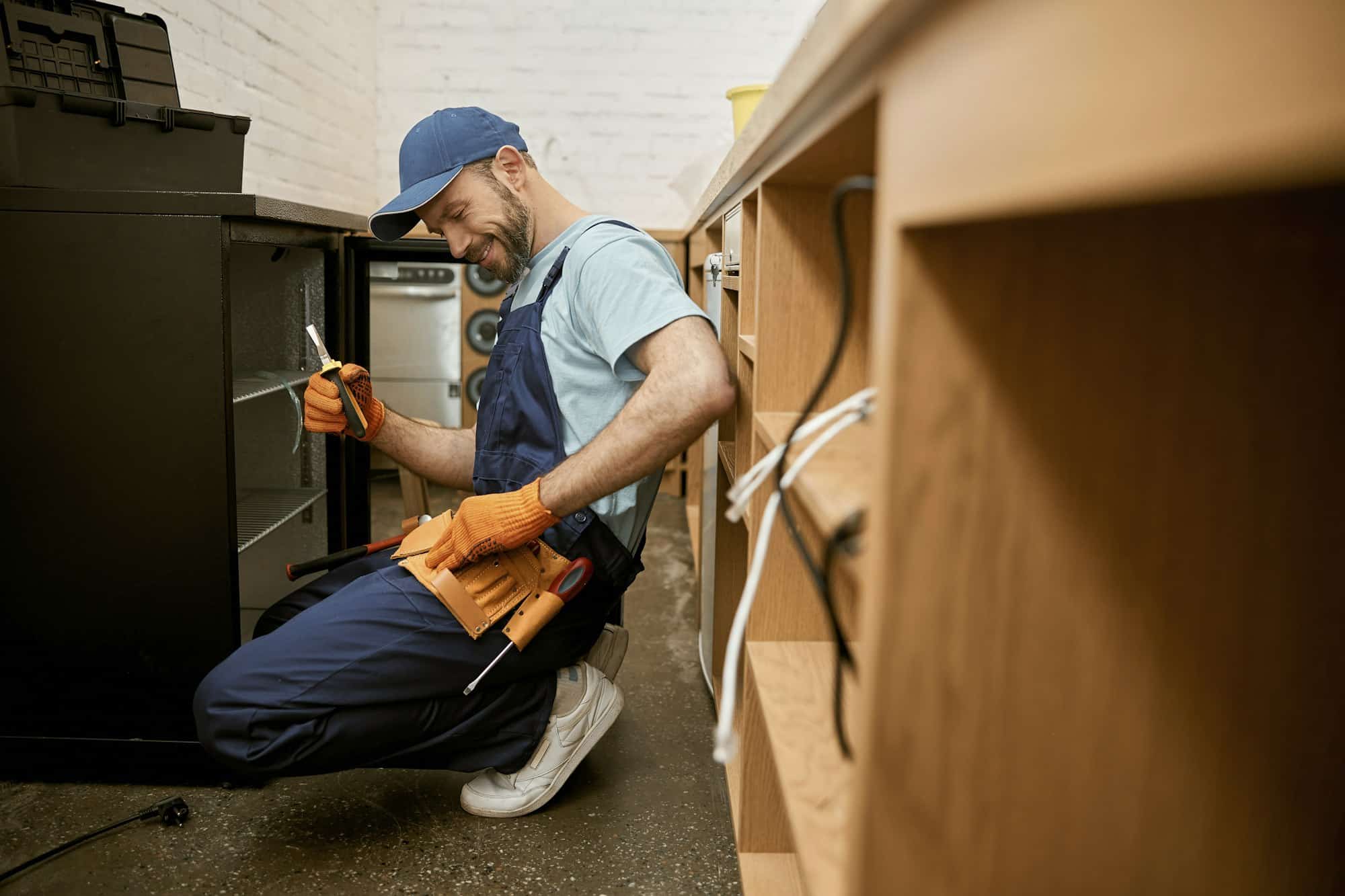 Cheerful young man fixing fridge in kitchen