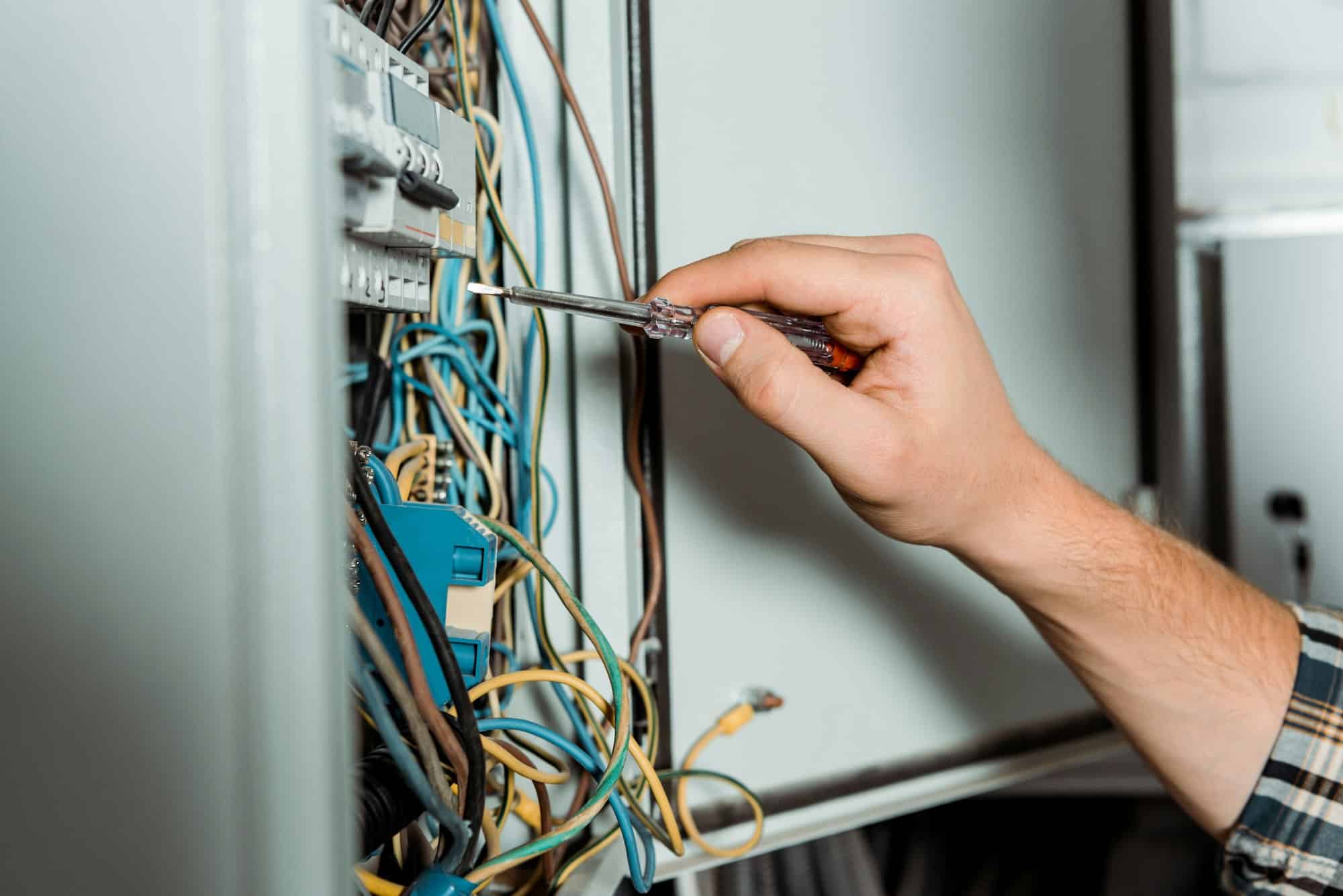 cropped view of electrician holding screwdriver near switchboard